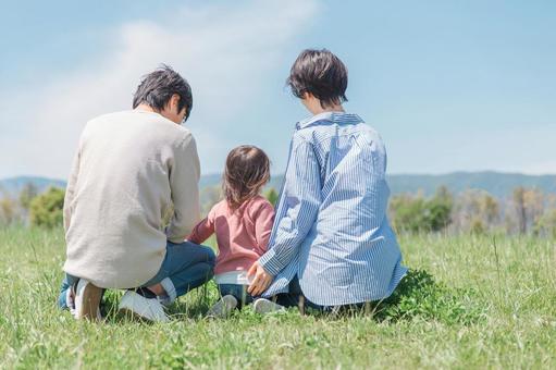 草原に座る家族の後ろ姿