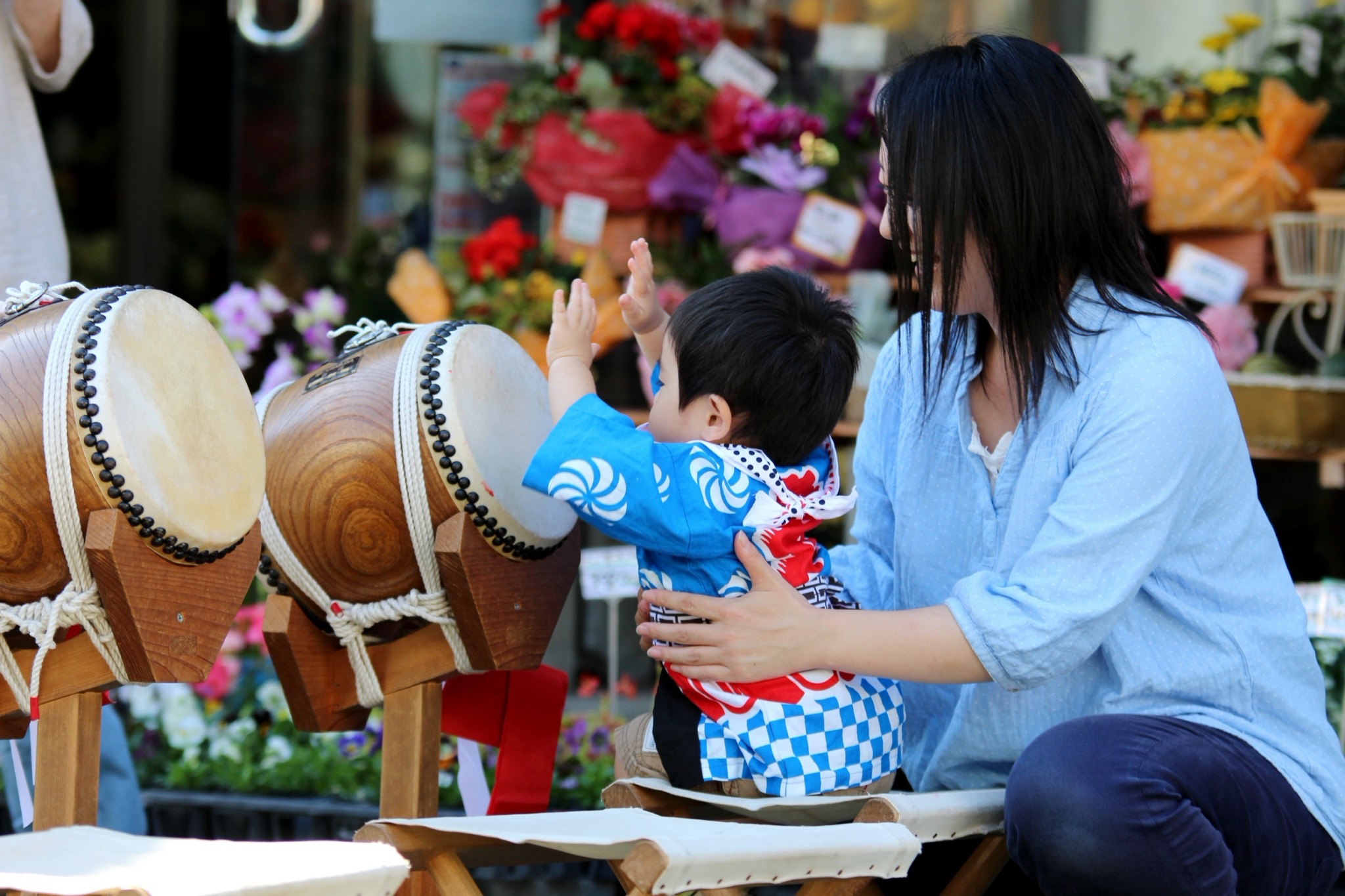 商店街の花屋の前、太鼓に手を伸ばす子どもと見守る母親
